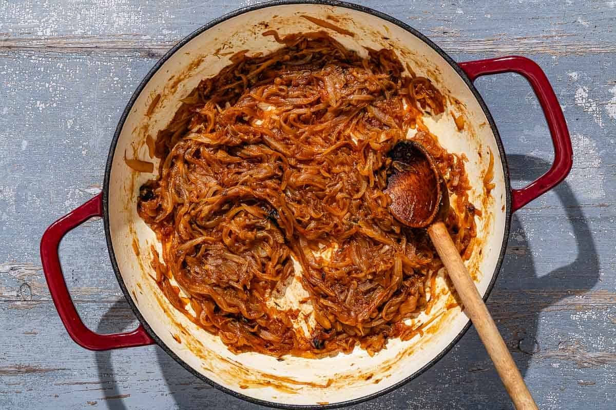 The caramelized onion mixture for pissaladière in a skillet with a wooden spoon.
