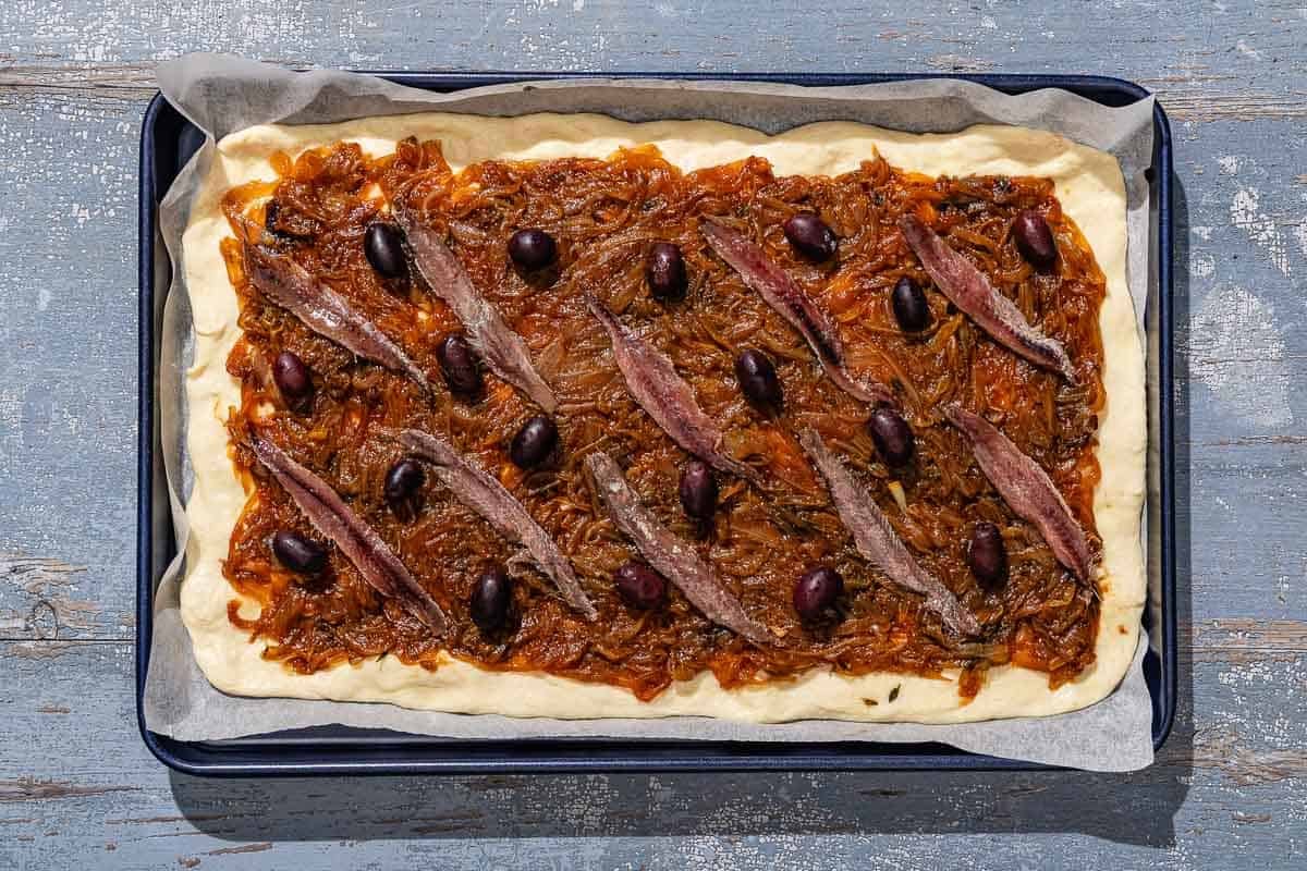 Unbaked pissaladière on a parchment lined sheet pan.