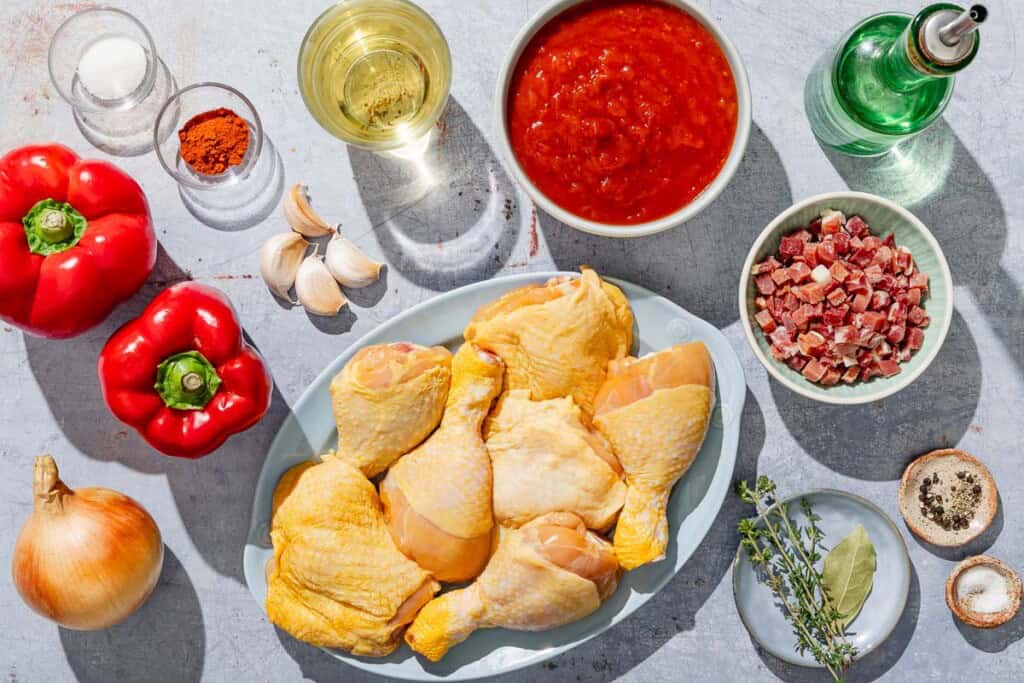 Ingredients for chicken and peppers olive oil, chicken drumsticks and thighs, salt, black pepper, onion, red bell peppers, diced pancetta, garlic, smoked Spanish paprika, fire-roasted tomatoes, white wine, sugar, bay leaf and a few sprigs of fresh thyme.