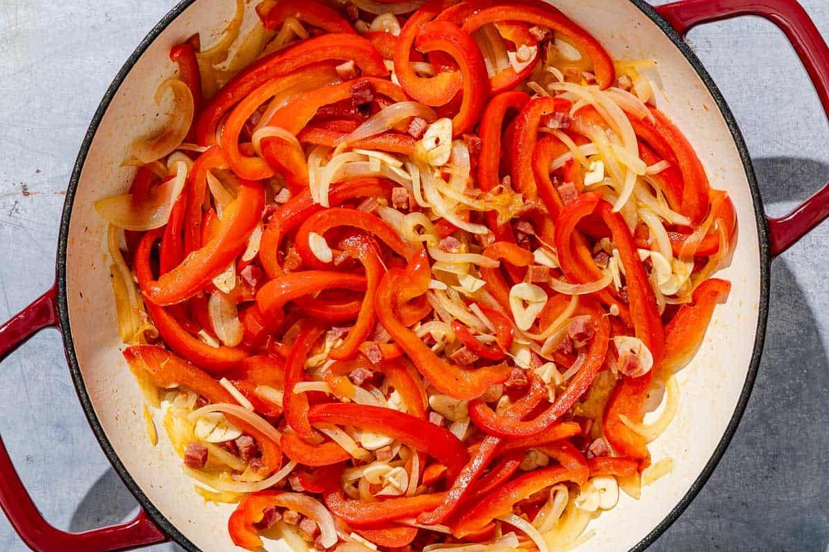 The onions and peppers for the chicken and peppers cooking together in a skillet.