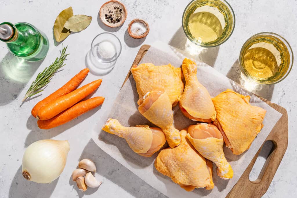 Ingredients for escabeche de pollo including chicken thighs and drumsticks, carrot, olive oil, salt, black pepper, yellow onion, garlic, white wine vinegar, white wine, sugar, fresh rosemary, and bay leaves.