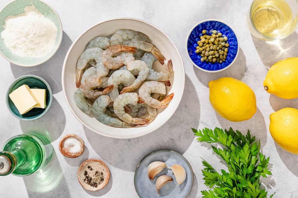 Ingredients for shrimp piccata including jumbo shrimp, salt, black pepper, flour, olive oil, butter, garlic, white wine, lemons, capers and parsley.