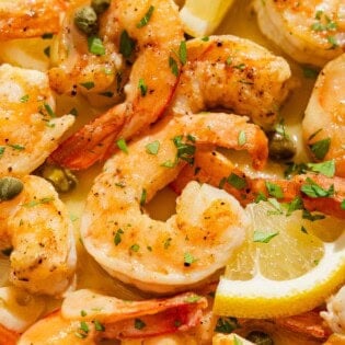 A close up of shrimp piccata with lemon wedges.