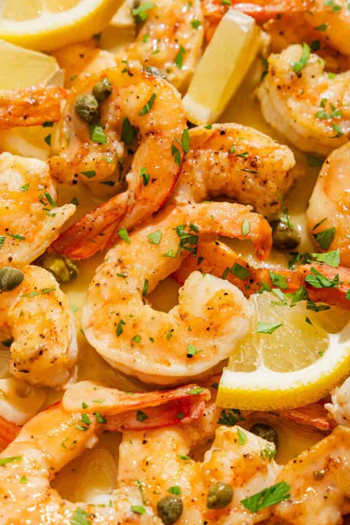 A close up of shrimp piccata with lemon wedges.