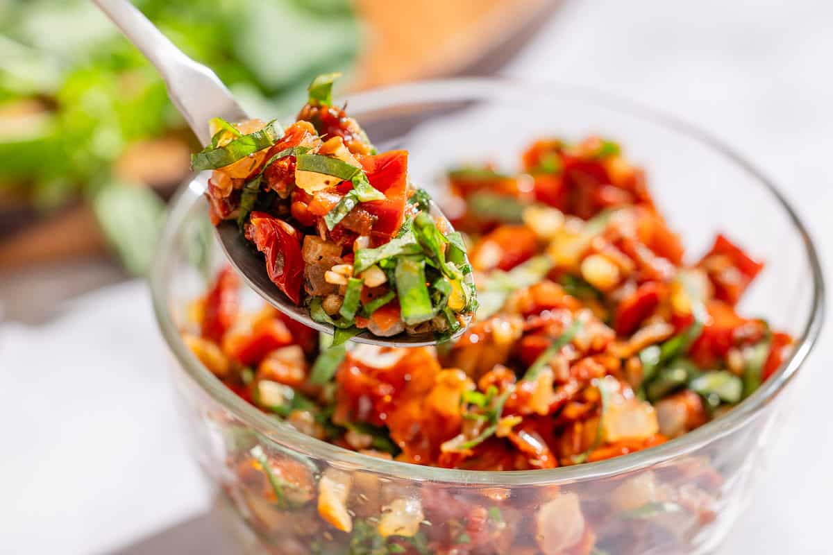 A spoonful of sun dried tomato salsa being lifted from a bowl of the salsa.