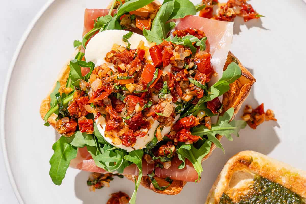 A open faced breakfast sandwich topped with sun dried tomato salsa on a plate.