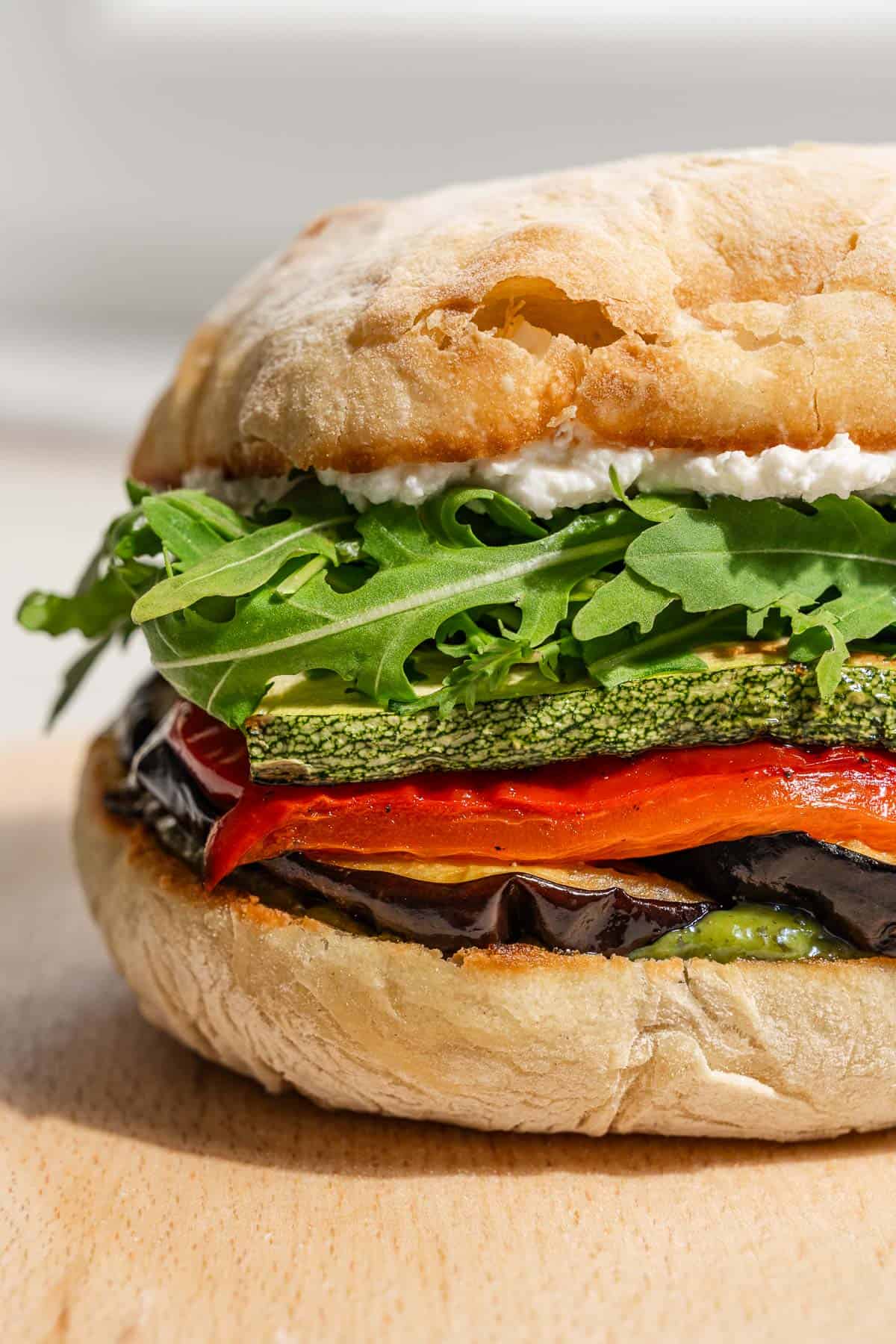 A close up of a roasted vegetable sandwich on a wooden tray.