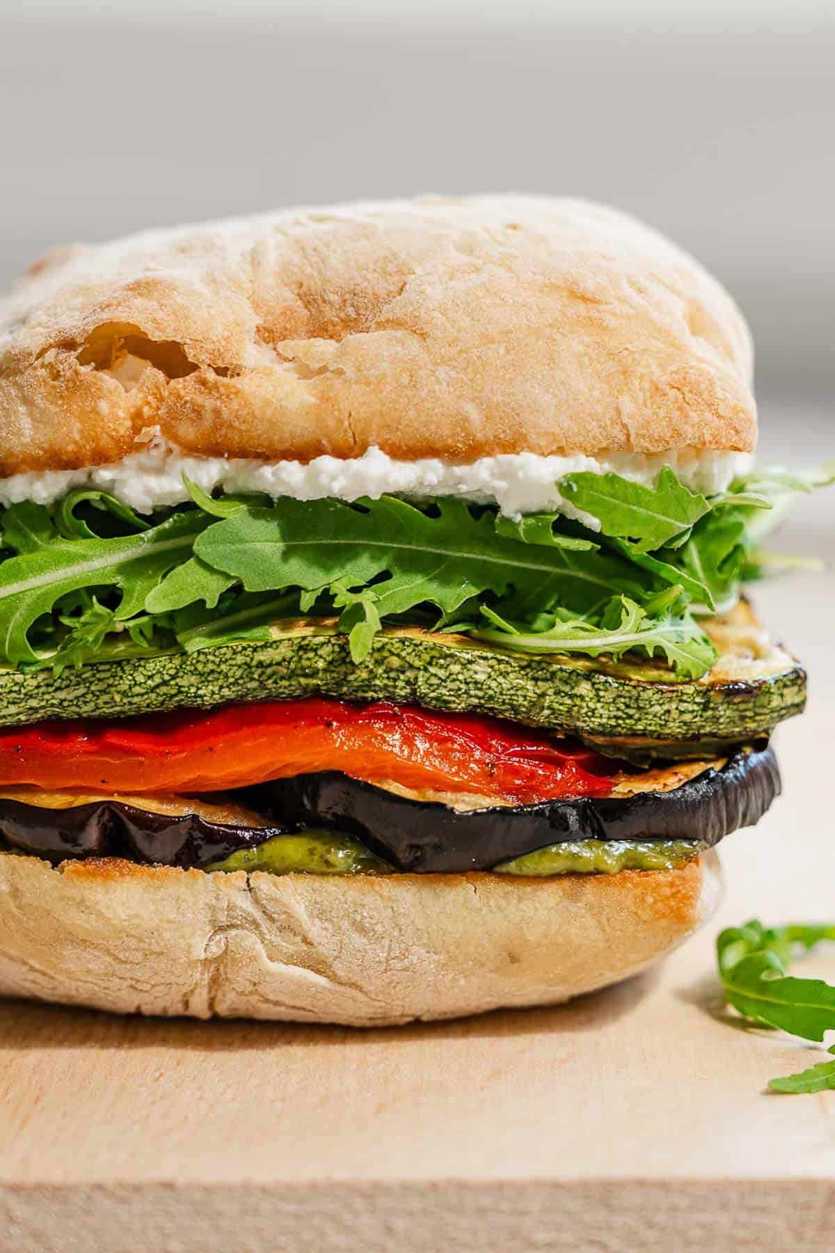A close up of a roasted vegetable sandwich on a wooden tray.
