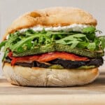 A close up of a roasted vegetable sandwich on a wooden tray.
