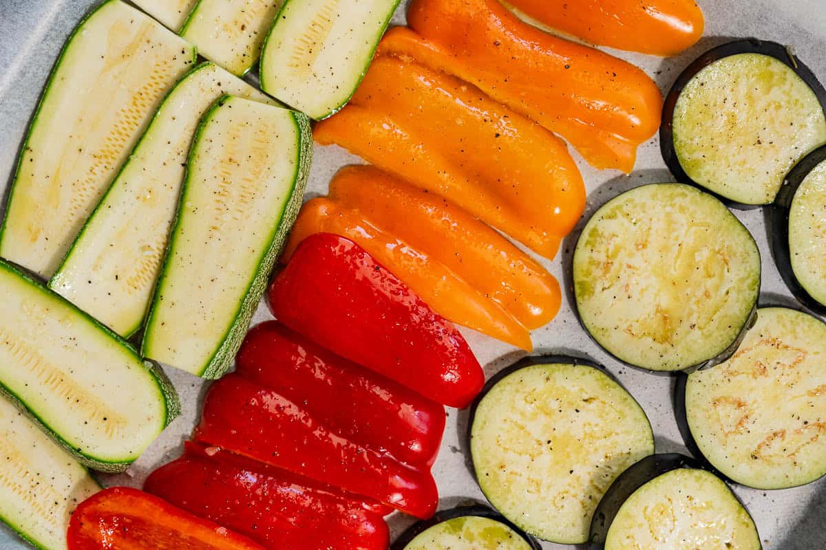 The sliced vegetables for the roasted vegetable sandwich recipe on a parchment lined sheet pan, seasoned and drizzled with olive oil.
