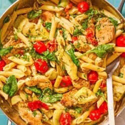 Chicken pasta in a tall-sided skillet with a spoon. Next to this is a kitchen towel and a small bowl of chopped parsley.