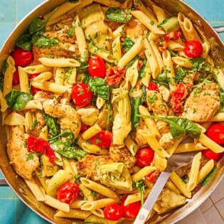 Chicken pasta in a tall-sided skillet with a spoon. Next to this is a kitchen towel and a small bowl of chopped parsley.