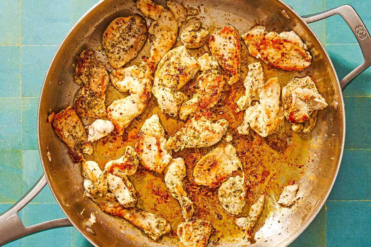 The seasoned pieces of chicken being browned in a skillet.