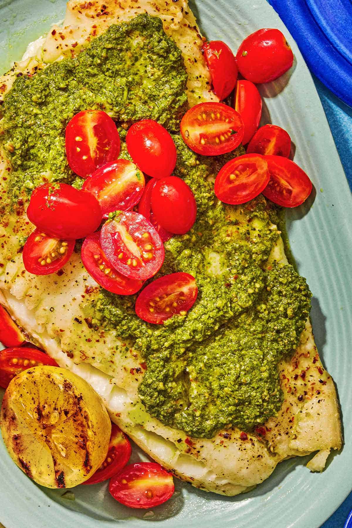Chilean sea bass topped with pesto and grape tomatoes on a platter.