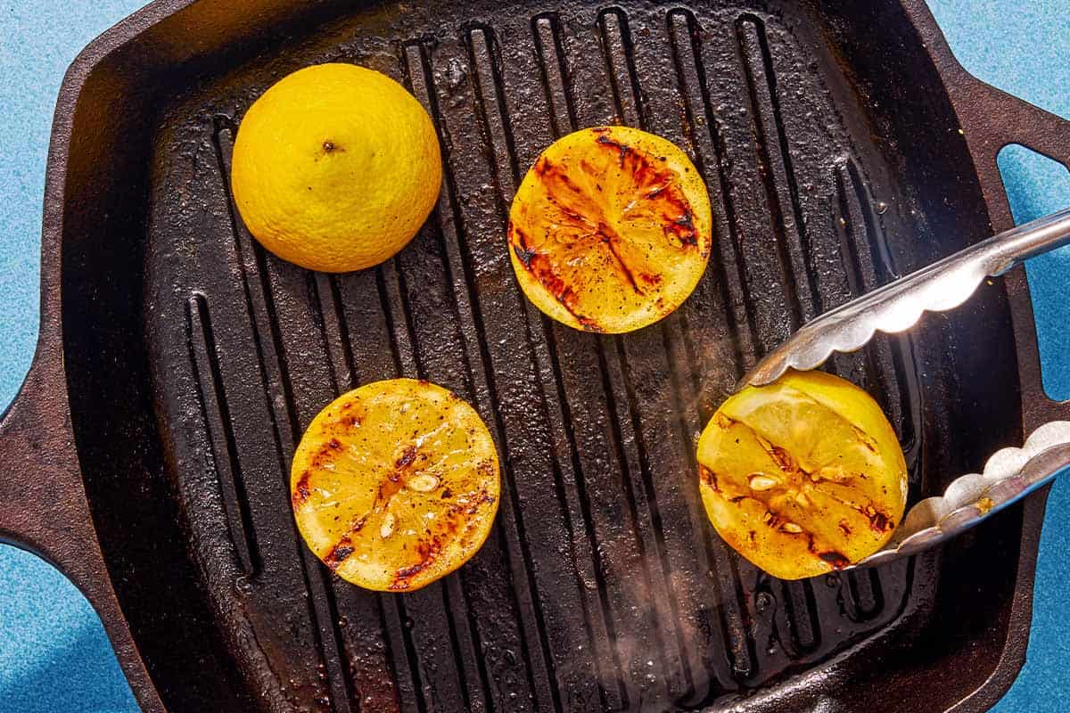 Lemon halves being cooked on a grill pan. One is being flipped over with a pair of tongs.