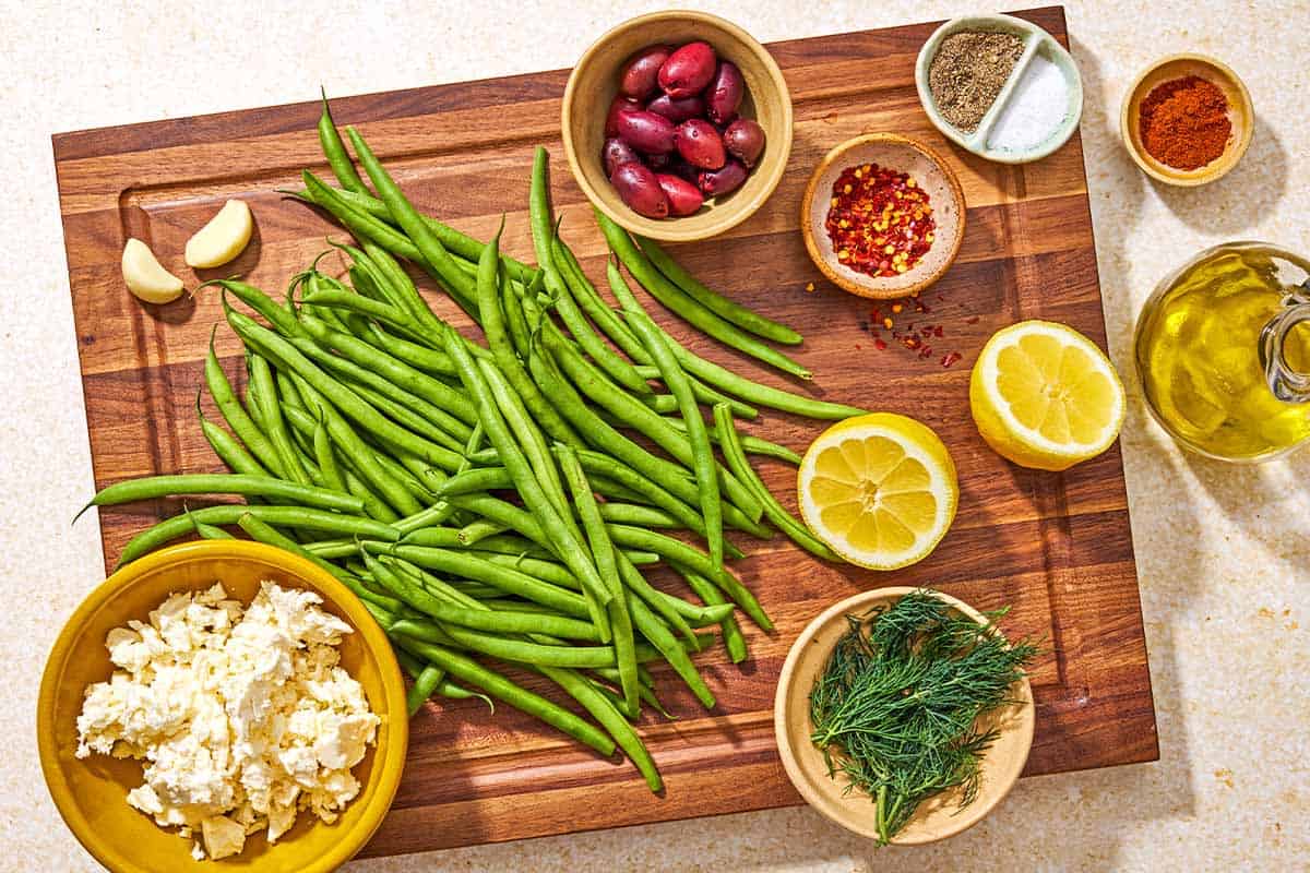 Ingredients for green bean salad including green beans, garlic, kalamata olives, feta, red pepper flakes, salt, black pepper, lemon, dill, sweet paprika and olive oil.