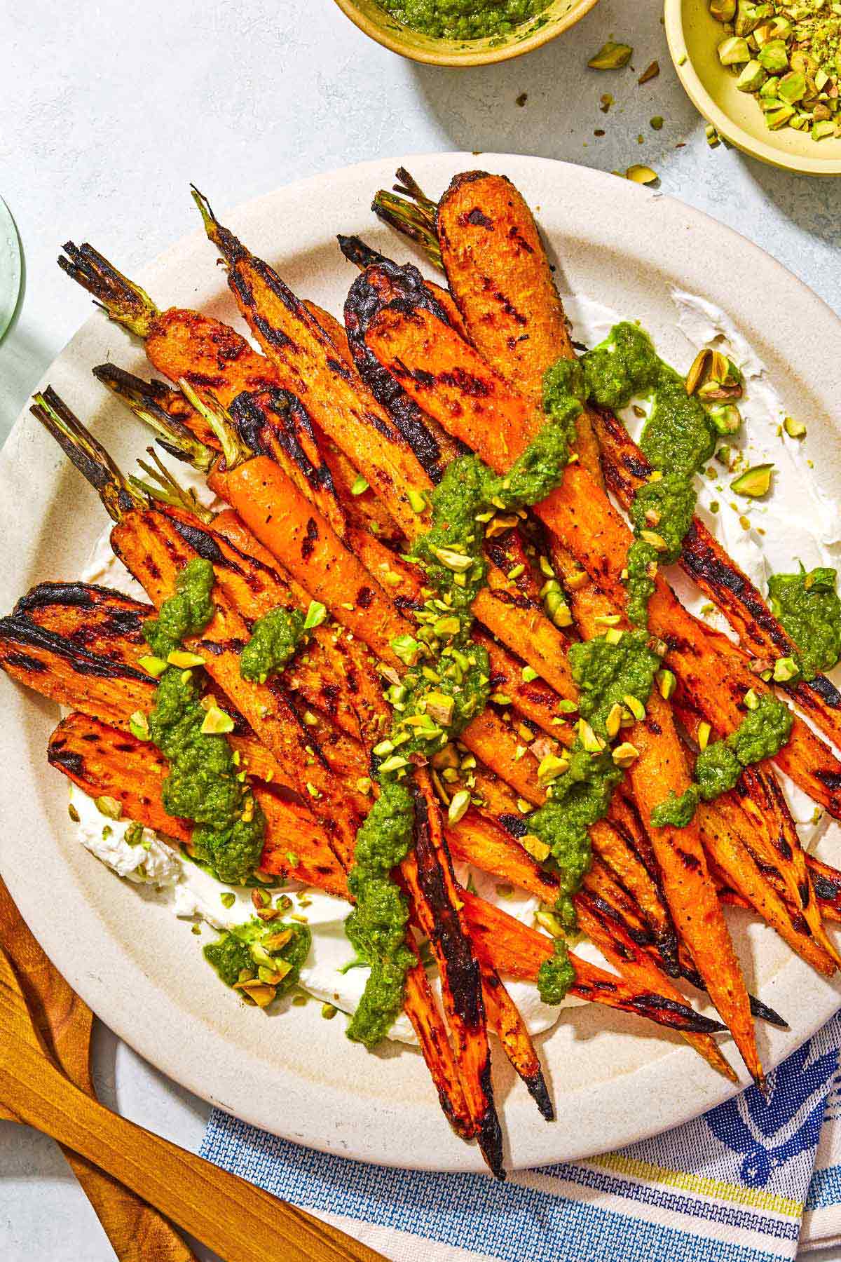 Grilled carrots with labneh topped with zhoug and chopped pistachios on a platter.