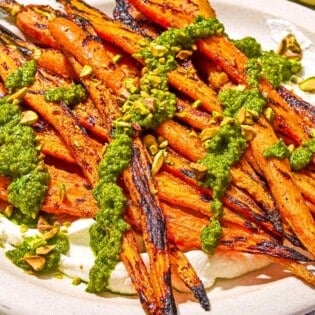 Grilled carrots with labneh topped with zhoug and chopped pistachios on a platter.