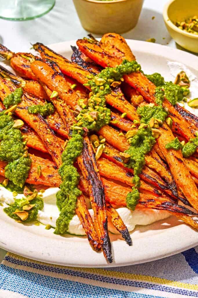 Grilled carrots with labneh topped with zhoug and chopped pistachios on a platter.