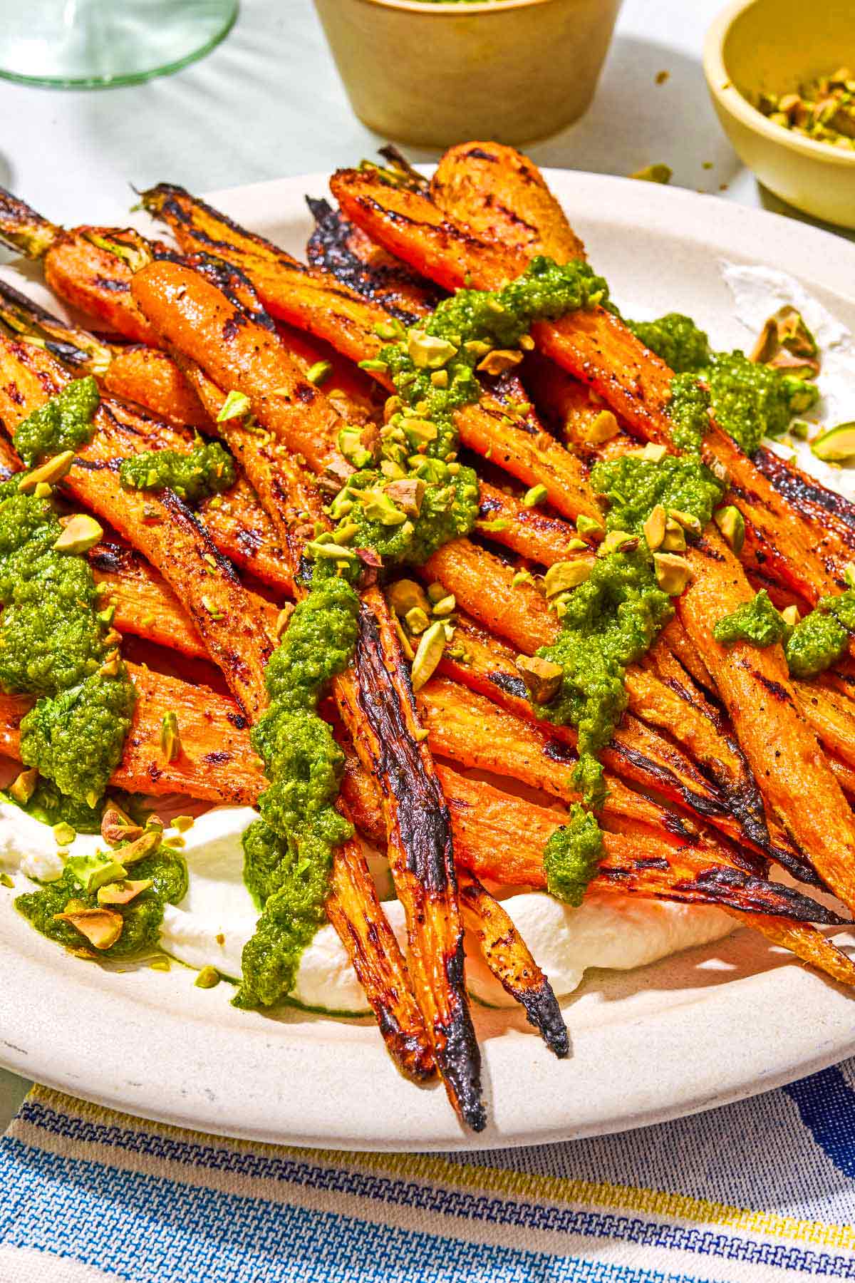 Grilled carrots with labneh topped with zhoug and chopped pistachios on a platter.