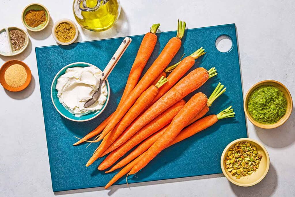 Ingredients for grilled carrots including whole carrots, olive oil, garlic powder, ground coriander, cround cumin, salt, black pepper, labneh, zhoug, and chopped pistachios.