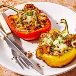 Two grilled stuffed peppers on a plate with a fork and knife.