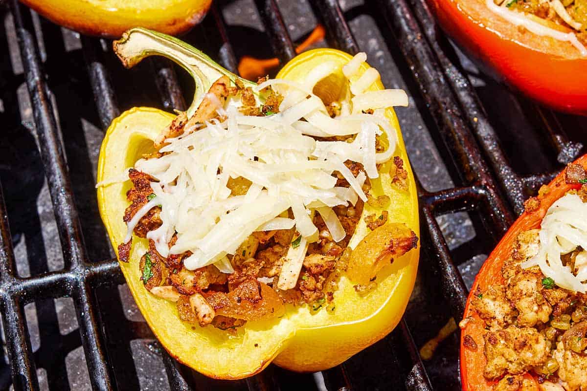 A close up of a stuffed grilled pepper just topped with shredded cheese on a grill.