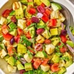 Avocado salad in a serving bowl with a spoon next to a small bowl of the dressing.
