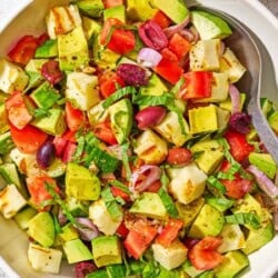 Avocado salad in a serving bowl with a spoon next to a small bowl of the dressing.