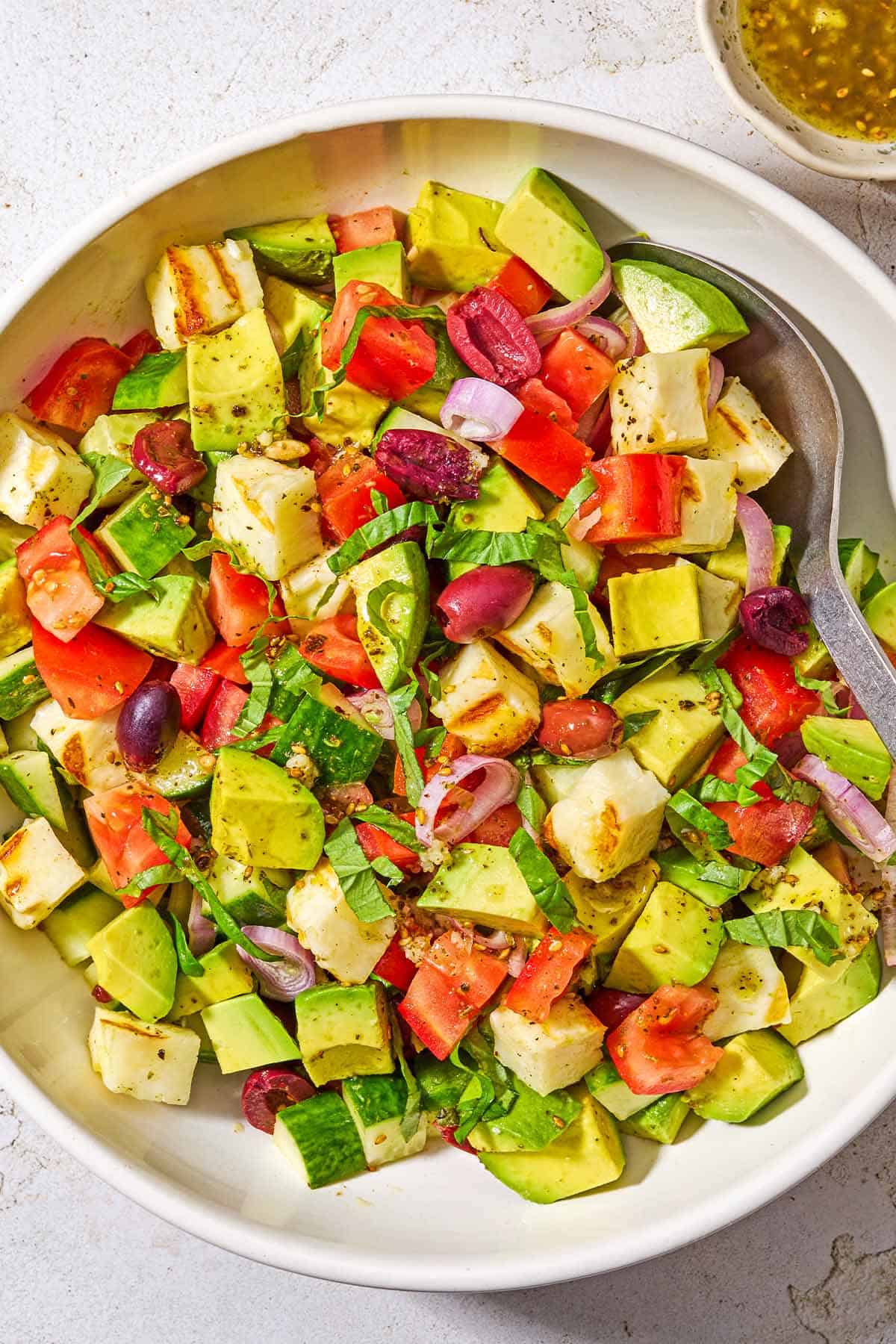 Avocado salad in a serving bowl with a spoon next to a small bowl of the dressing.