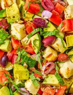 A close up of avocado salad made with tomatoes, cucumbers, za'atar, halloumi and olives.