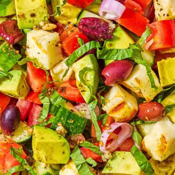 A close up of avocado salad made with tomatoes, cucumbers, za'atar, halloumi and olives.