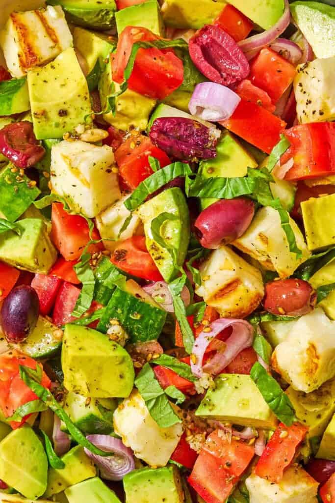 A close up of avocado salad made with tomatoes, cucumbers, za'atar, halloumi and olives.