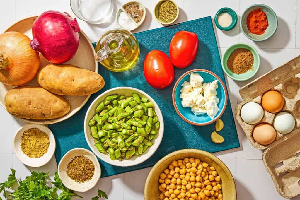 Ingredients for potato hash including potatoes, onions, garlic, salt, black pepper, chickpeas, asparagus, allspice, za'atar, dried oregano, paprika, coriander, sugar, tomatoes, feta, parsley, white vinegar and eggs.