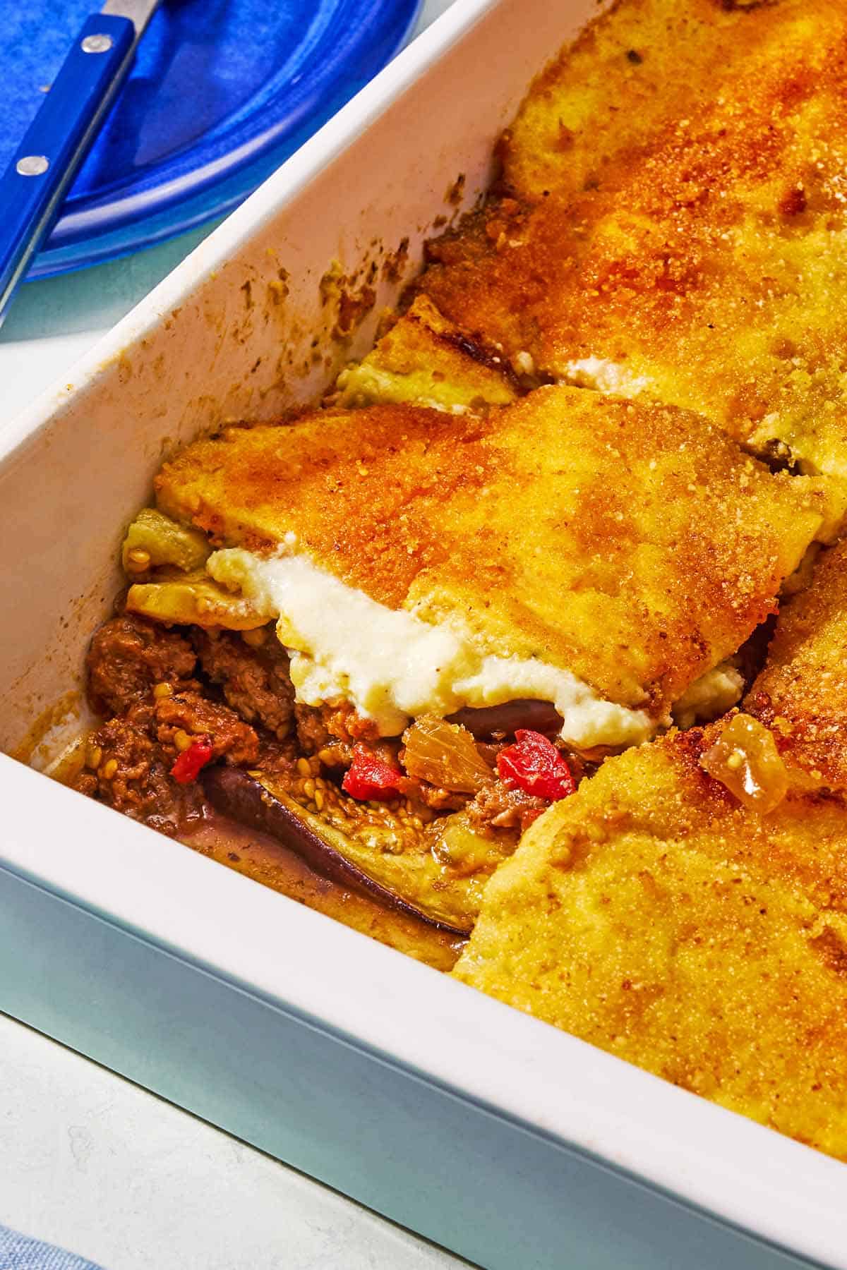 A close up of the moussaka with one piece removed in a baking dish.