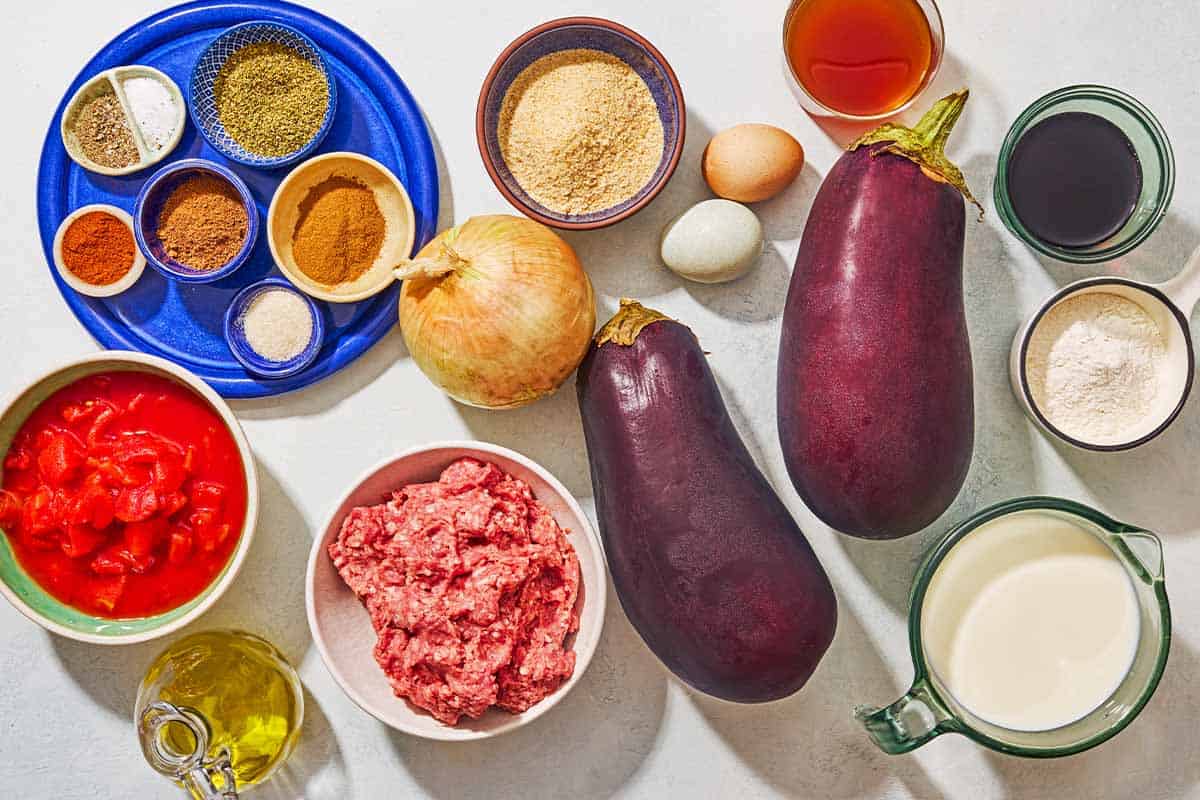 Ingredients for moussaka including eggplant, salt, black pepper, olive oil, breadcrumbs, onion, ground beef, dried oregano, cinnamon, nutmeg, paprika, red wine, diced tomatoes, sugar, beef broth, all purpose flour, milk and eggs.