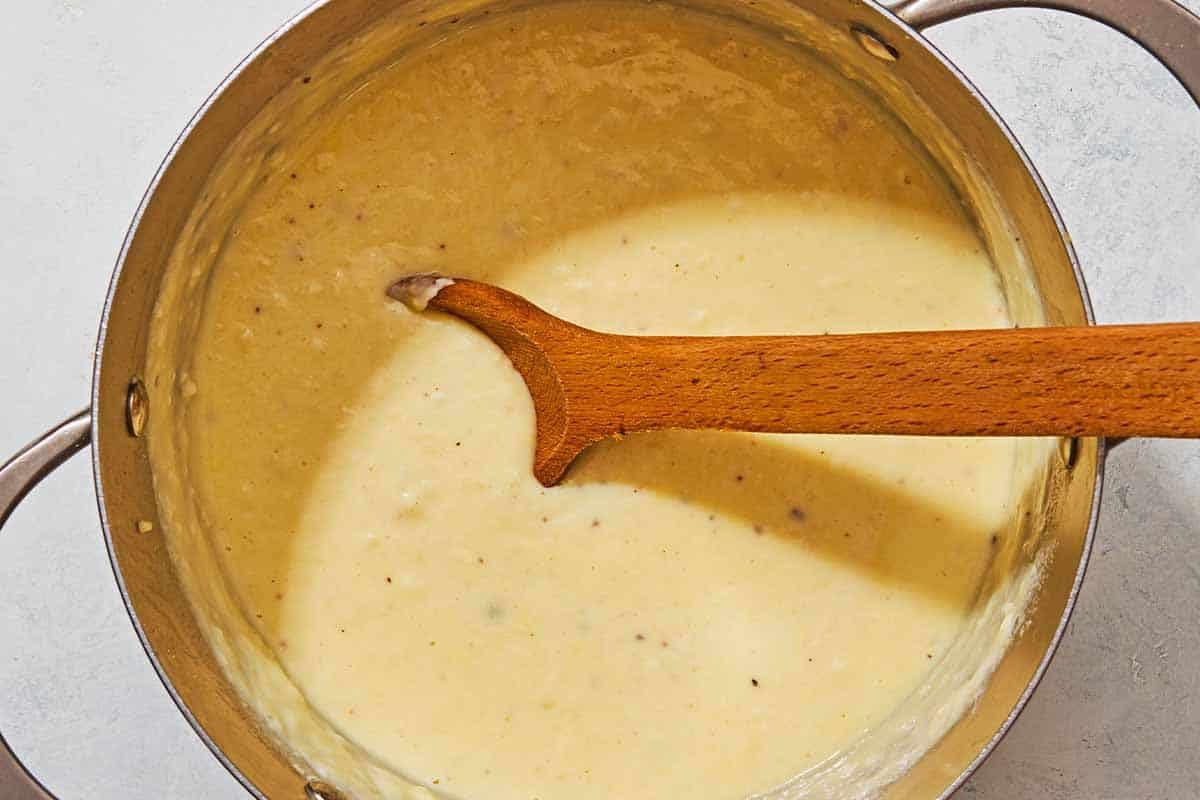 The bechamel for the moussaka in a saucepan with a wooden spoon.