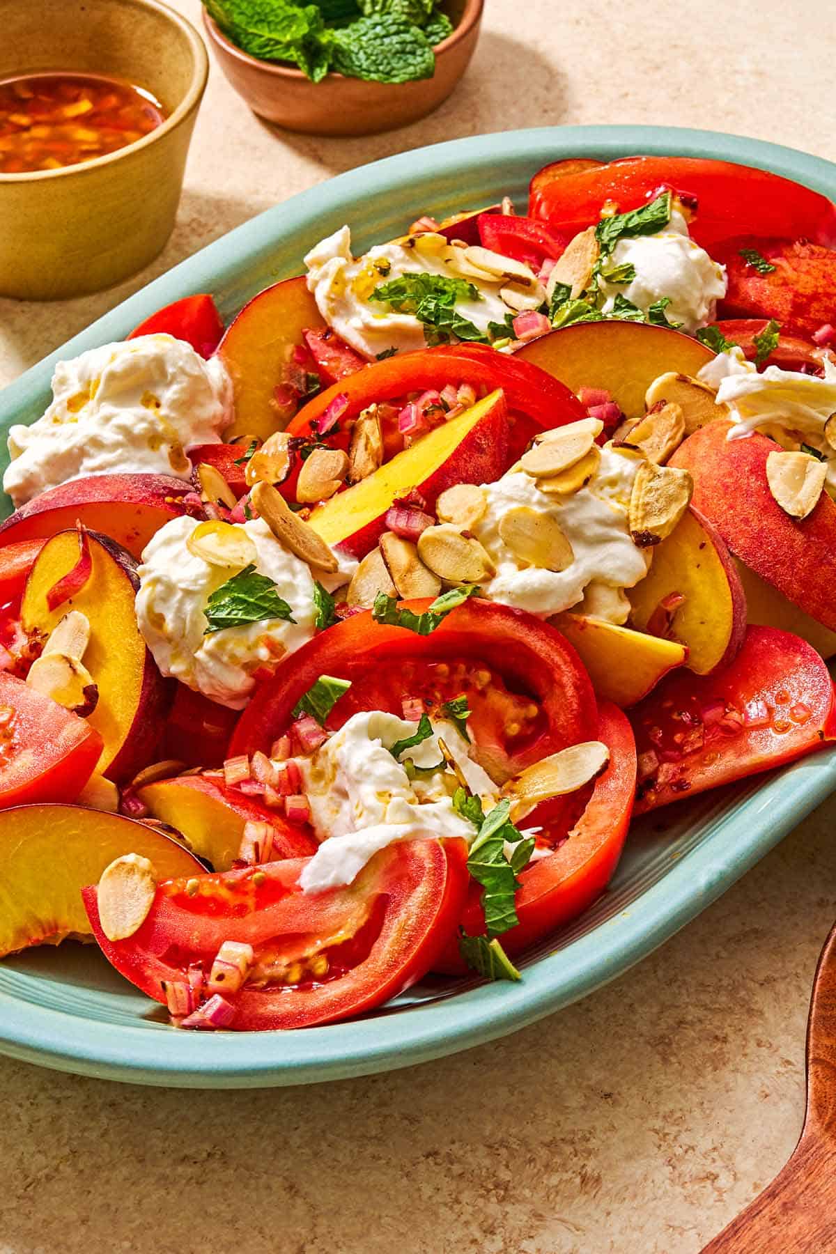 Peach burrata salad on a platter next to small bowls of the dressing and mint leaves.