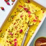 Persian ice cream in a loaf pan with a scoop next to a bowl of honey with a honey dipper.