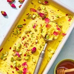Persian ice cream in a loaf pan with a scoop next to a bowl of honey with a honey dipper.