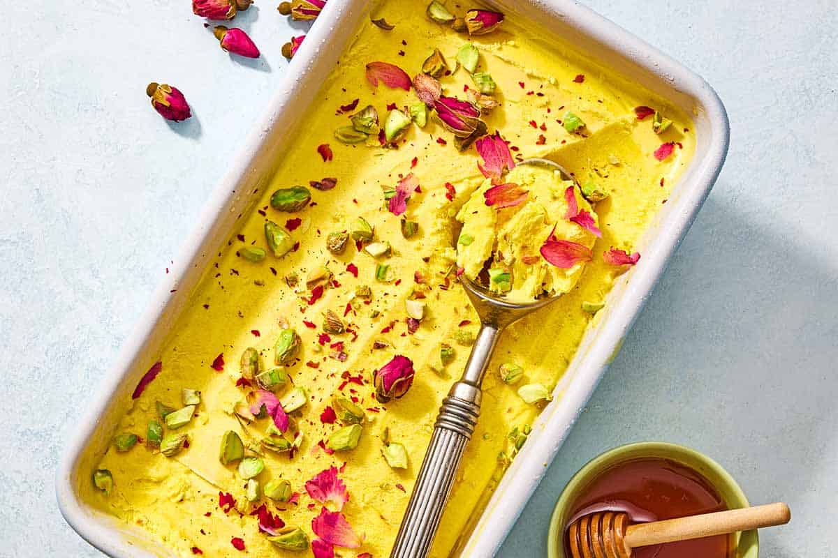 Persian ice cream in a loaf pan with a scoop next to a bowl of honey with a honey dipper.