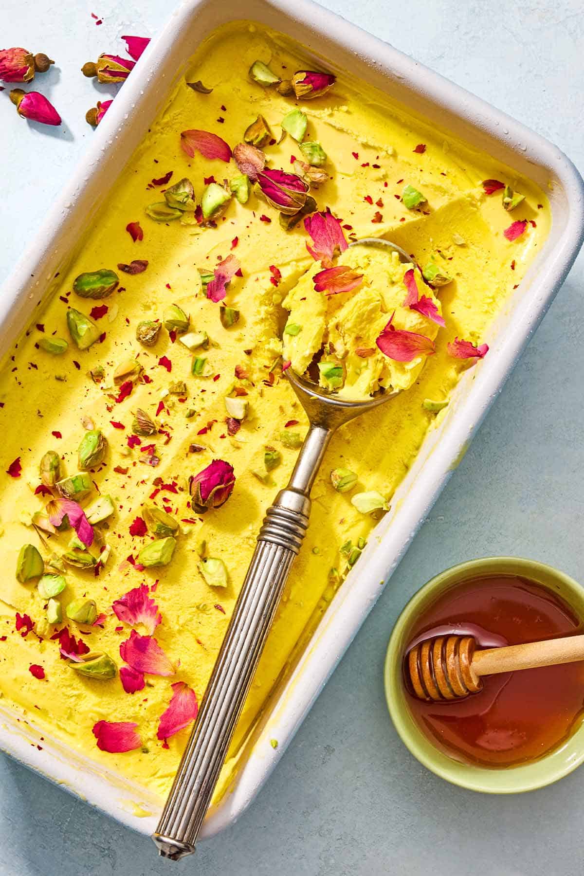 Persian ice cream in a loaf pan with a scoop next to a bowl of honey with a honey dipper.