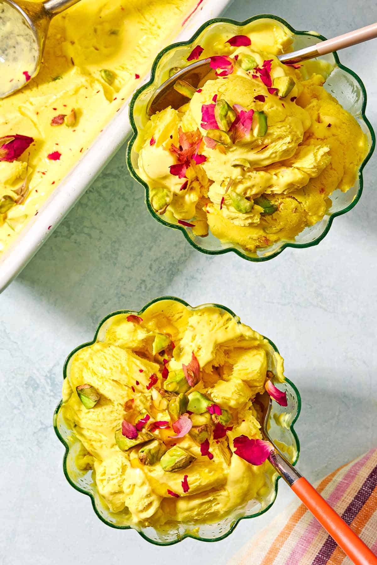 2 goblets with persian ice cream (Bastani Sonnati) and spoons. The ice cream is topped with pistachio and rose petals.
