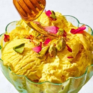 A goblet with persian ice cream being drizzled with honey from a honey dipper.