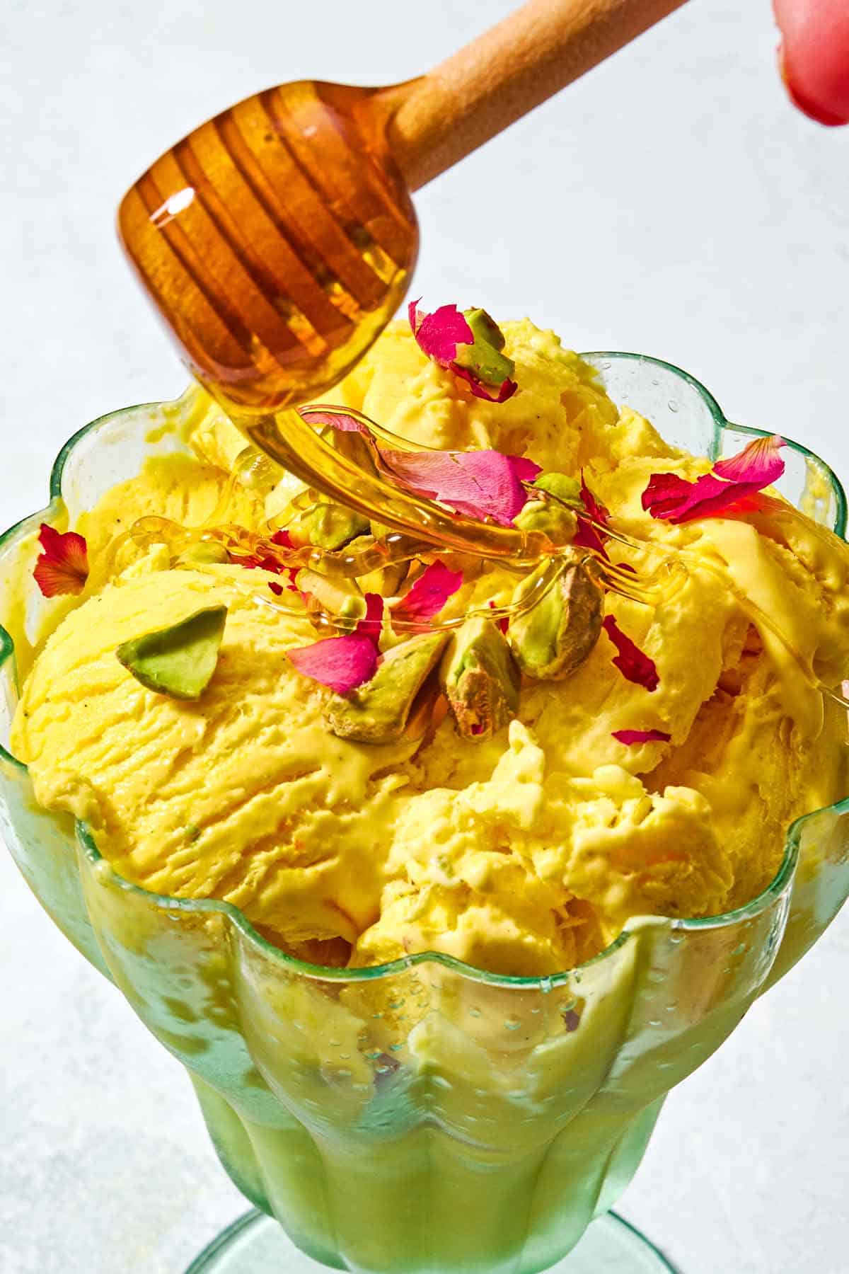 A goblet with persian ice cream being drizzled with honey from a honey dipper.