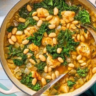 White bean and kale soup in a pot with a ladle next to a bottle oil and a lemon half.