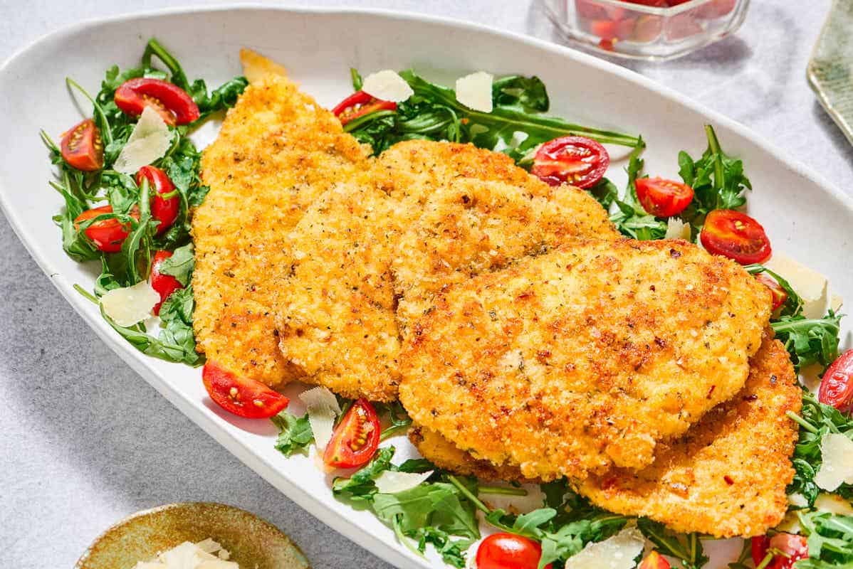 Chicken milanese cutlets on a bed of arugula salad on a serving platter.