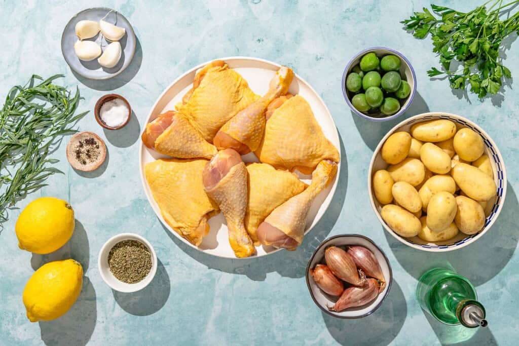 Ingredients for the chicken and potatoes recipe including chicken thighs and legs, lemons, garlic, herbs de provence, salt, black pepper, olive oil, yellow potatoes, shallots, olives, parsley, and tarragon.