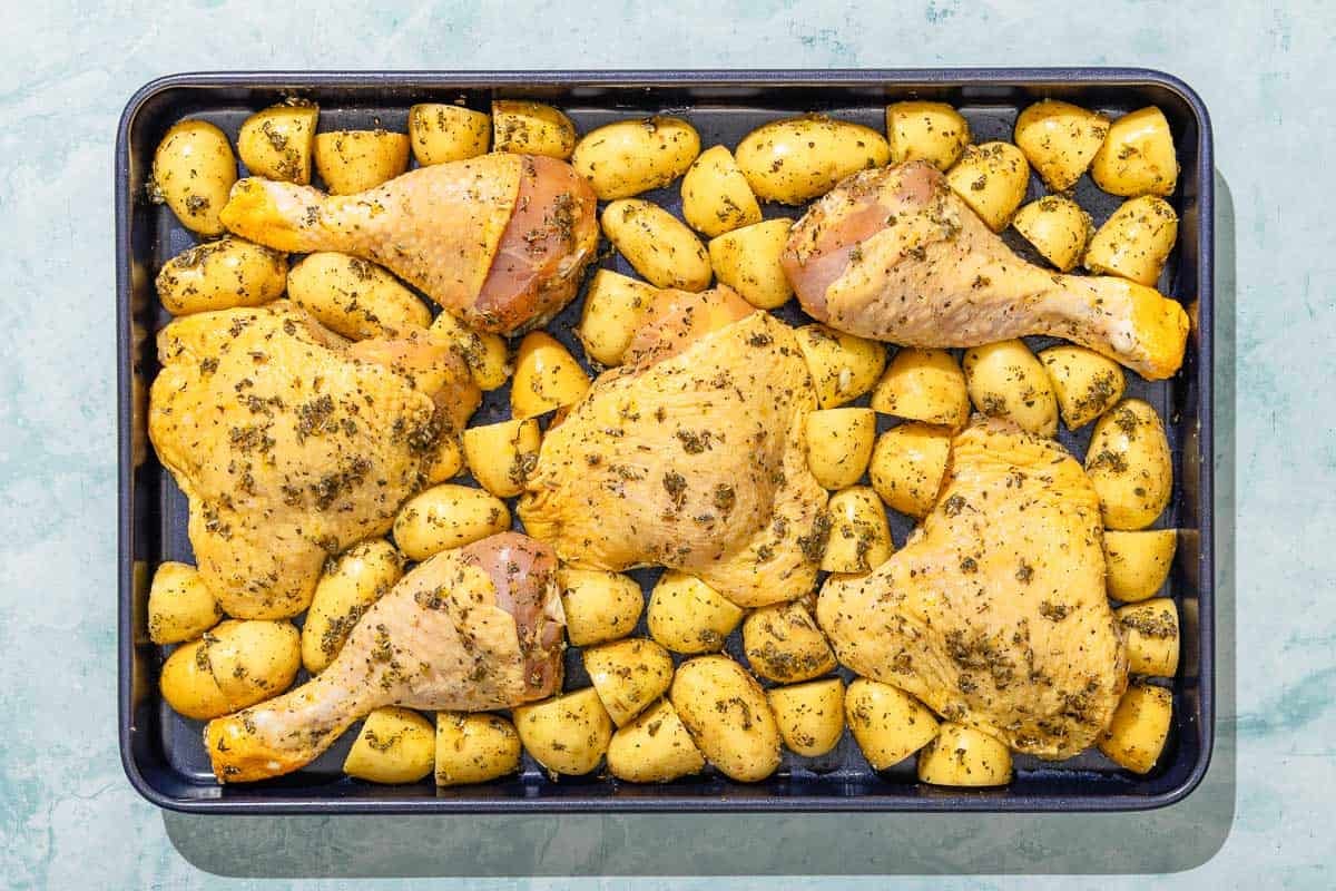 The uncooked chicken and potatoes on a sheet pan.