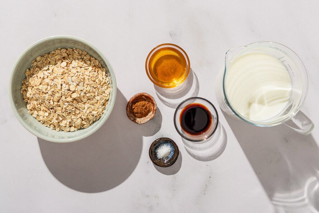 Ingredients for oatmeal including rolled oats, milk, vanilla extract, ground cinnamon, salt, and honey.